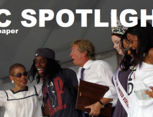 A group of people smiling and celebrating on stage with a spotlight above.