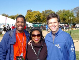 Three people smiling outdoors on a sunny day with trees in the background.