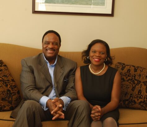 A man and woman sitting on a couch, smiling at the camera.