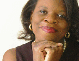 Portrait of a smiling woman with hands gently resting under her chin.