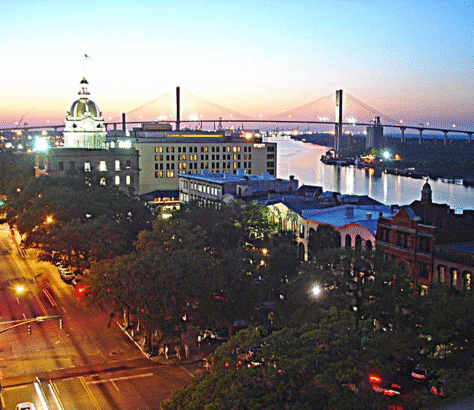 Evening cityscape with a suspension bridge and illuminated buildings.