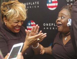 Two women joyfully high-fiving at an event with a OnePlate America backdrop.