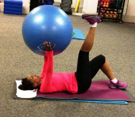 Woman exercising with a blue stability ball on a mat indoors.