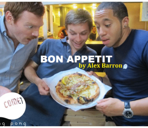 Three men excitedly admire a delicious plate of food in a cozy kitchen.
