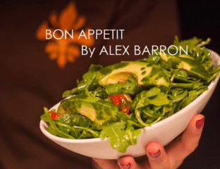 Fresh green salad in a white bowl held by hands.