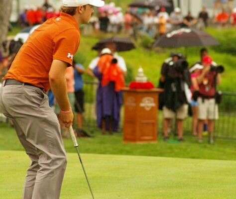 Golfer putting on green with spectators in the background.