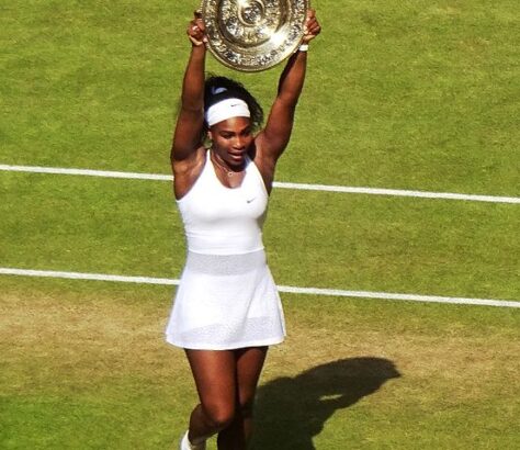 Tennis player celebrating with a trophy on a grass court.