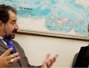 Two people in discussion beside a world map on the wall.