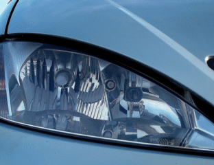 Close-up of a car's sleek headlight on a light blue body.