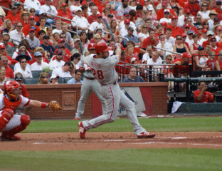 Baseball player swings to hit the ball during a game with a crowd in the stands.