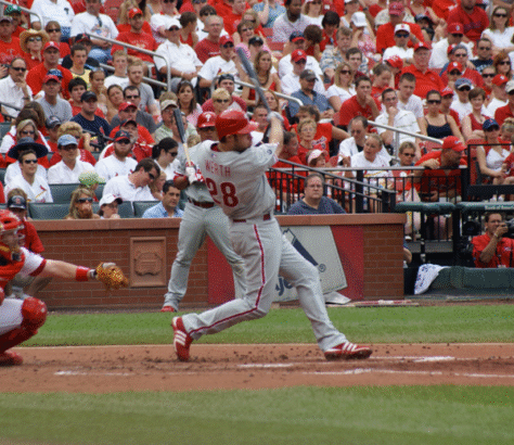 Baseball player swings to hit the ball during a game with a crowd in the stands.