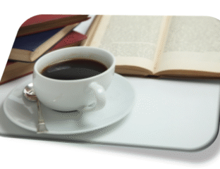 A cup of coffee beside an open book and stacked books.