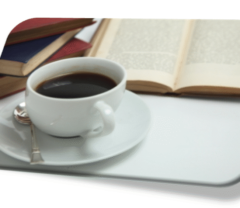 A cup of coffee beside an open book and stacked books.