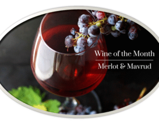 A glass of red wine with grapes, highlighting Merlot and Mav wine varieties.