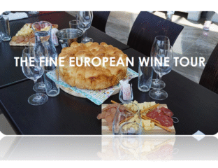 A rustic European bread and charcuterie spread with wine glasses on a dark table.
