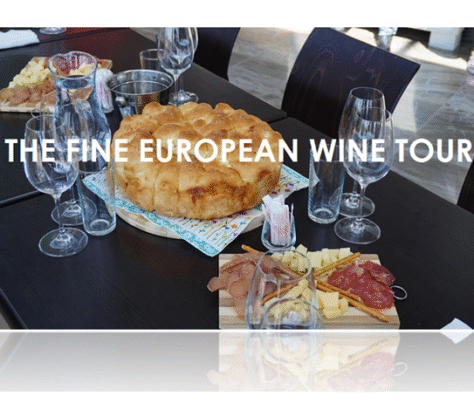 A rustic European bread and charcuterie spread with wine glasses on a dark table.