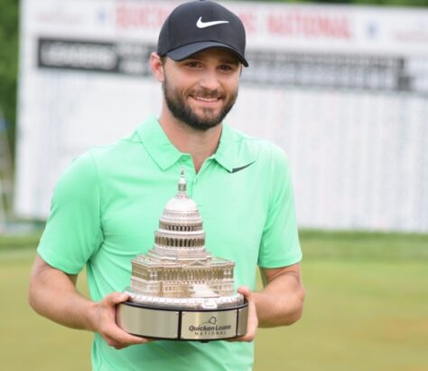 A smiling golfer in a green shirt holding a trophy shaped like the US Capitol.