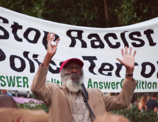 A man raises his hands in front of an anti-racism protest banner.