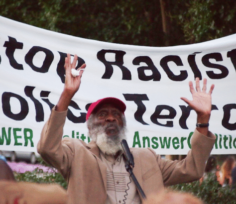 A man raises his hands in front of an anti-racism protest banner.