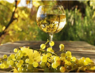 A glass of white wine with grapes on a wooden surface outdoors.