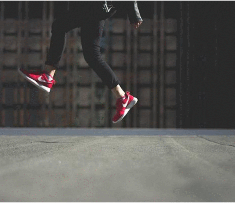 Person jumping mid-air wearing red sneakers against a dark background.