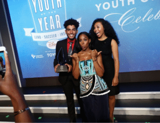 Three people posing on a stage at a Youth of the Year award event.