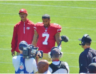 Two football players in red jerseys on the field surrounded by cameras and media.