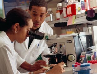 Two scientists examining samples through a microscope in a lab.