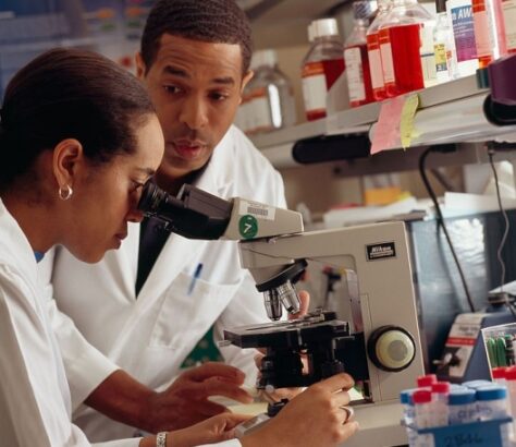 Two scientists examining samples through a microscope in a lab.
