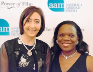 Two women smiling at a formal event with branded backdrops.