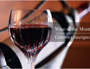 A glass of red Cabernet Sauvignon wine with a bottle in the background.