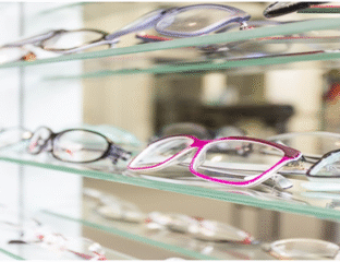 Brightly colored eyeglasses displayed on glass shelves in an optical store.