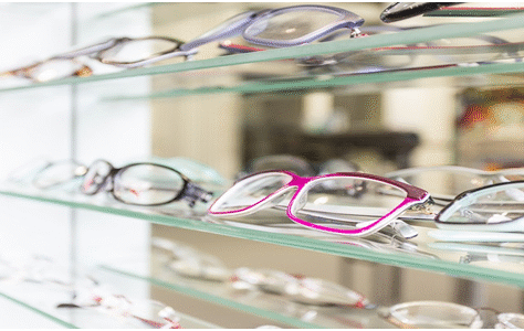Brightly colored eyeglasses displayed on glass shelves in an optical store.