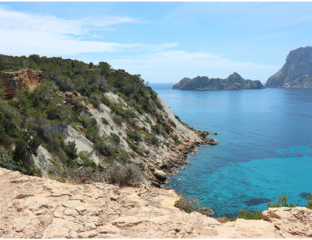 Rocky coastline with clear blue sea and distant islands under a bright sky.