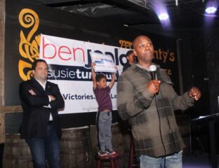 Man speaking at an event with a child and another man on stage.