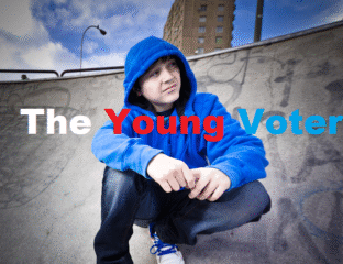 A young person in a blue hoodie crouching outdoors against an urban backdrop.