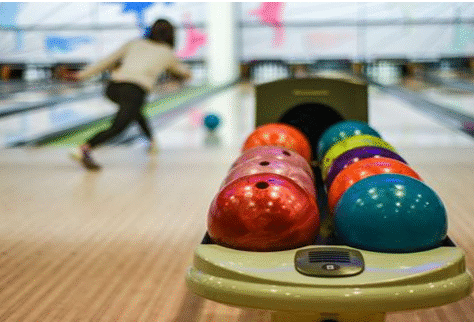 Bowling balls lined up with a person bowling in the background.