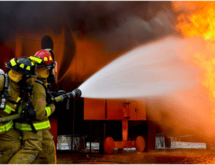 Firefighter sprays water on a blazing building fire at night.