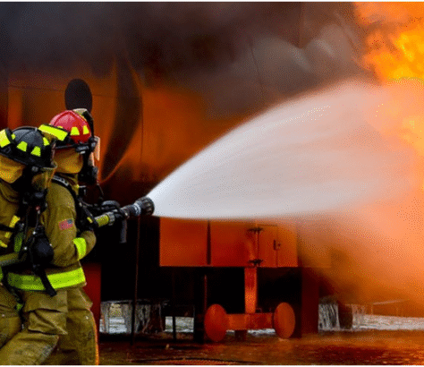 Firefighter sprays water on a blazing building fire at night.