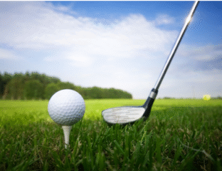 A golf ball on a tee with a golf club ready to hit it on a grassy field.