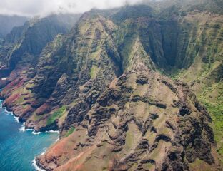Aerial view of rugged mountains with lush greenery and a rocky coastline.