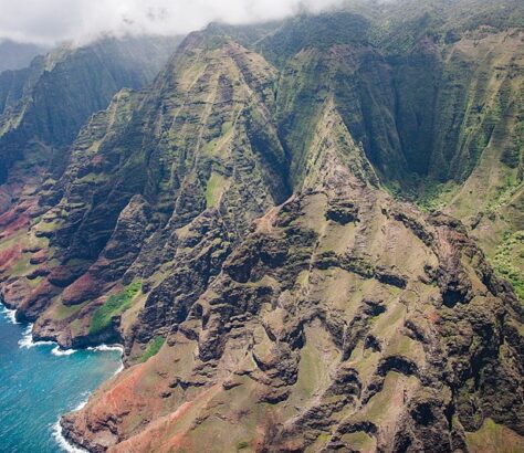 Aerial view of rugged mountains with lush greenery and a rocky coastline.