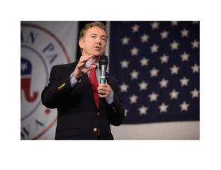A man speaking at a political event with a U.S. flag backdrop.