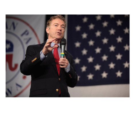A man speaking at a political event with a U.S. flag backdrop.