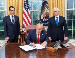 President signing a document in the Oval Office with officials present.