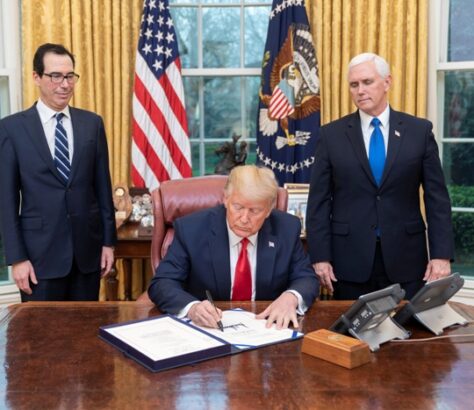 President signing a document in the Oval Office with officials present.