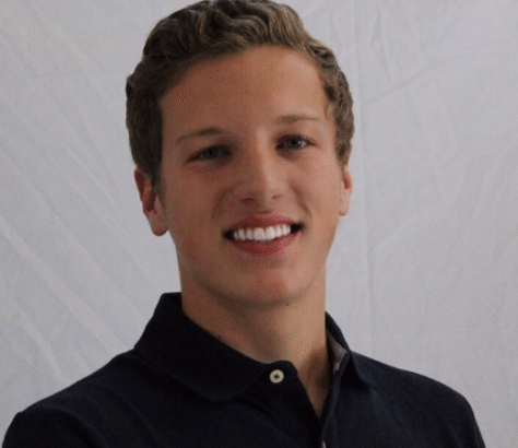 Young man smiling in a black polo shirt against a plain background.