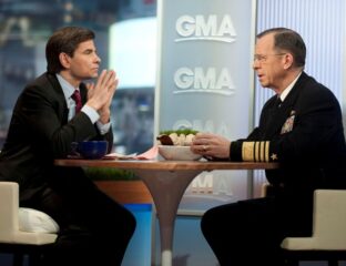 Two men engaged in a serious conversation on a talk show set.