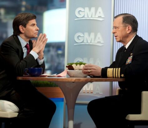 Two men engaged in a serious conversation on a talk show set.