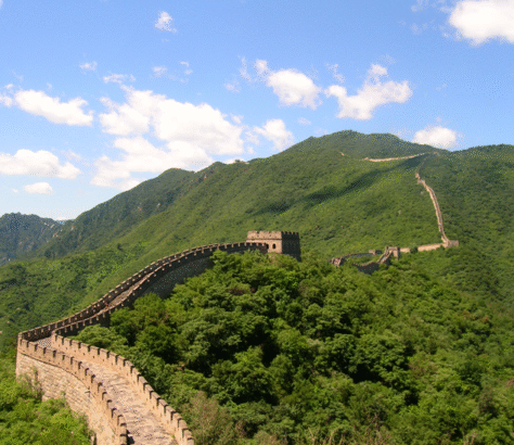 The Great Wall of China stretches across lush green mountains under a bright blue sky.